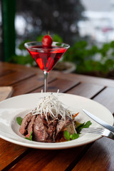 Top view of thai style marbled beef salad with sweet alcoholic strawberry cocktail on summer terrace