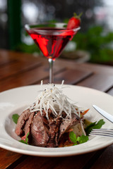 Top view of thai style marbled beef salad with sweet alcoholic strawberry cocktail on summer terrace