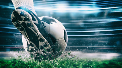 Voetbalscène bij nachtwedstrijd met close-up van een voetbalschoen die de bal met kracht raakt