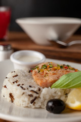 Steamed piece of salmon with boiled basmati rice in a white dish, served on a rustic wooden table