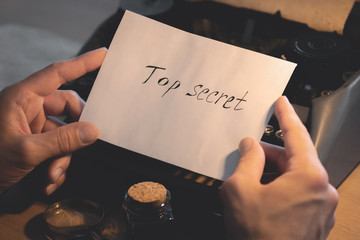 Top secret document letter in a detective spy agent hands on a table background.