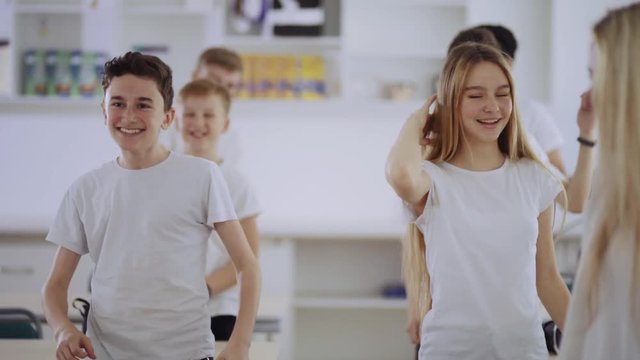 Happy school children dancing of fun in the middle of classroom. Friendly pretty students relaxing at a break in a school.
