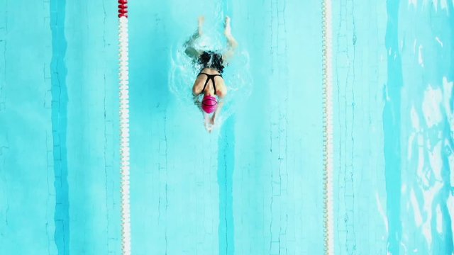 Woman swimmer doing the breaststroke in a clear blue pool passing below the camera in a swimming lane