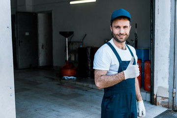 handsome bearded car mechanic in cap standing and showing thumb up