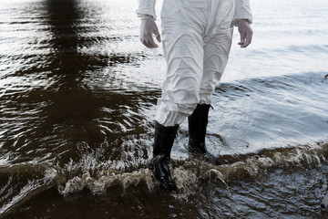 partial view of water inspector in protective costume and boots standing in river