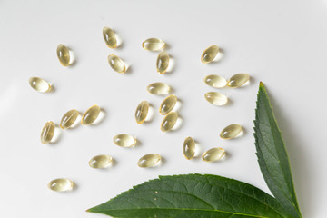 CBD Pills on White Background with Plant Leaves, Vitamin D Pills, Yellow Capsules, Supplements