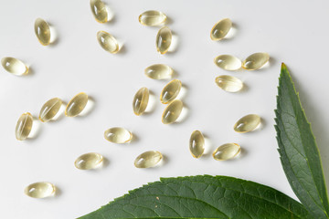 CBD Pills on White Background with Plant Leaves, Vitamin D Pills, Yellow Capsules, Supplements