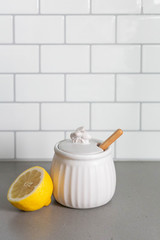 White Ceramic Honey Pot with Wooden Honey Dipper and Lemon Slice, White Subway Tile Background in Kitchen