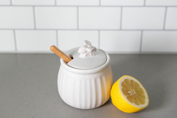 White Ceramic Honey Pot with Wooden Honey Dipper and Lemon Slice, White Subway Tile Background in Kitchen