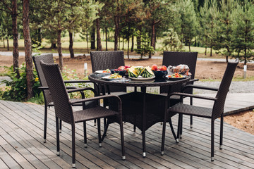 A lovely table in the garden or park served with delicious fruit and veggies for summer picnic. Fruit and vegetables on the table with five chairs.