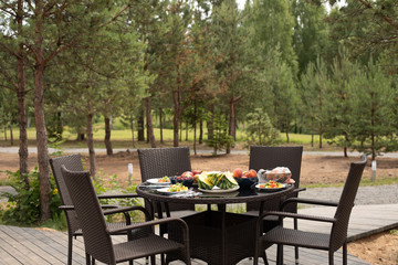 A lovely table in the garden or park served with delicious fruit and veggies for summer picnic. Fruit and vegetables on the table with five chairs.