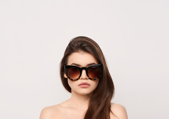 Naklejka premium sunglasses girl, close up studio shot of beautiful fashion young woman model with long hair looking at camera . while posing against clean white blank copy space wall for your content