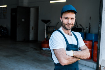 happy bearded car mechanic standing with crossed arms