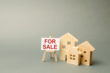 Three houses and a stand with the inscription FOR SALE. Advertising campaign. purchase of real estate. Announcement of the sale and attracting buyers. Construction and sale of housing and offices.