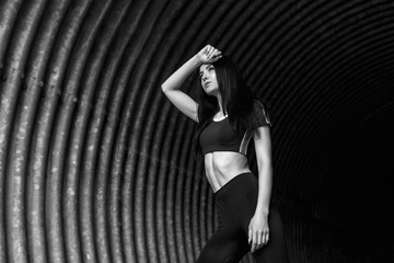 Sports woman rest after run in fashion sportswear on tunnel urban background. Fitness model working out outdoor. Young beautiful slim brunette girl in trendy leggings and top. Black and white.