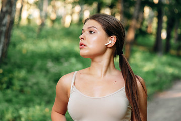 Close up portrait of a lovely young fitness girl listening to music through wireless earphones outdoors