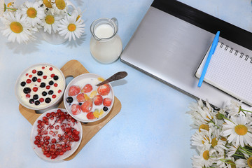Strawberry yogurt, milk and ripe currant berries and strawberries next to a closed computer on a light background.