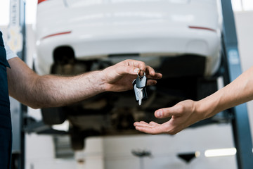 cropped view of auto mechanic giving key to man in garage