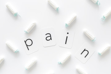 Fototapeta premium Gynaecologist and menstruation concept with tampons and pain word pattern on white background top view