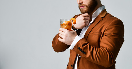 Young modern man bearded clubber in fashion suit holds the glass with fresh cocktail mohito and...