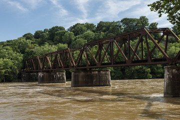 Beautiful vintage steel railroad bridge crossing a brown river with green trees