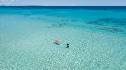 Couple on vacation at the beach, one of them with an inflatable mattress. Formentera crystal clear water