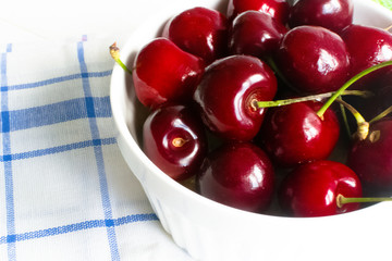 Fresh cherry in white ceramic bowl on wooden white background.