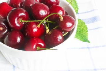 Fresh cherry in white ceramic bowl on wooden white background.