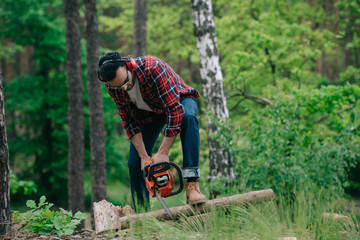 Obraz premium lumberjack in plaid shirt and denim jeans cutting wood with chainsaw in forest