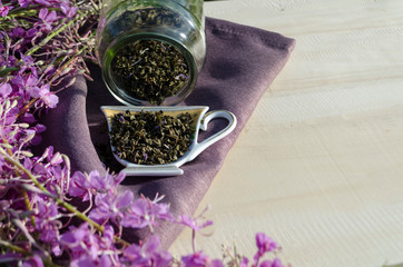 flower tea Ivan-tea wormwood in a glass jar and a cup on a purple napkin on a wooden background. soft focus.