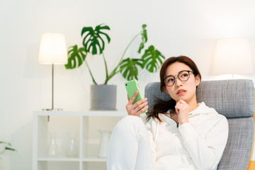 部屋でスマホを見る女性　考える