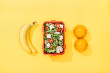 top view of lunch box with salad near bananas and oranges