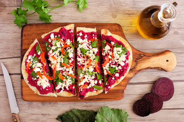 Beet hummus flat bread with feta cheese. Above scene on a paddle board against a wood background. Healthy eating concept.