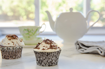 Cupcakes with chocolate for traditional afternoon tea with china teapot and cup in background, selective focus