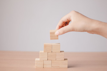 Hand putting wood cube on top of wood block stacking as step stair.business growth to success.