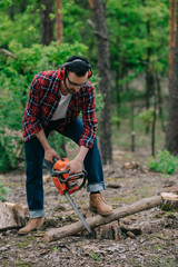 lumberjack in noise-canceling headphones cutting wood with chainsaw in forest