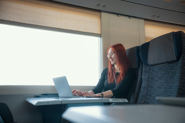 A ginger woman sitting in the train and working with a laptop