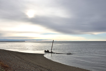 Bote semi hundido al atardecer subiendo la marea con cielo nublado de fondo