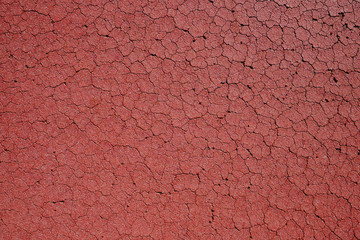 Red cracked surface of an old playing field, top view detail.