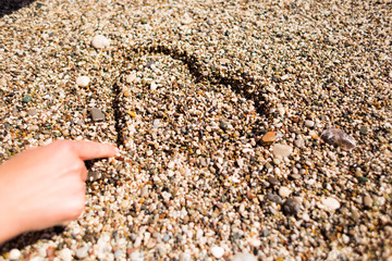 A girl sits on the beach and draws a heart in the sand.