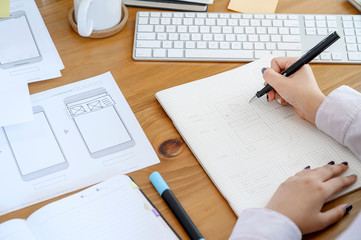 Female designer  drawing and designing UI UX application or website on paperwork at office.