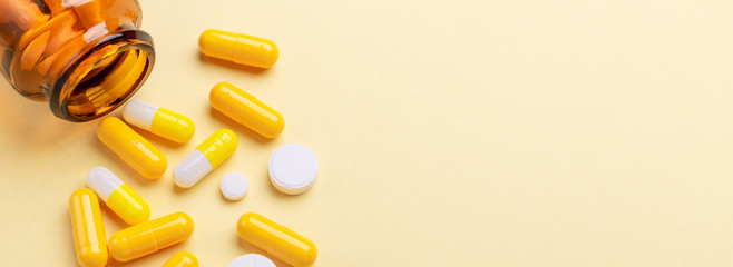 Multicolor tablets and pills capsules from glass bottle on yellow background Health care Close-up...
