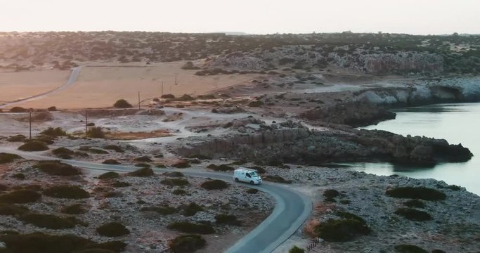Flying above tourist car driving along the desert rocky coastline of the island at the sea. Drone view of the bus driving to its destination at the seaside. Cyprus, south of Europe. Cape Greco