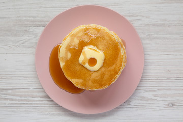 Stack of homemade pancakes with butter and maple syrup on a pink plate, overhead view. Top view, from above, flat lay. Close-up.