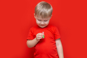 small boy blonde hair is going to eat many tablets pills in his hands, dangerous without adult people, Red clothes and red background