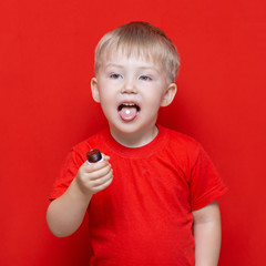 small three years old boy wants to eat pill, tablet on his tongue, can bottle in hand. red background