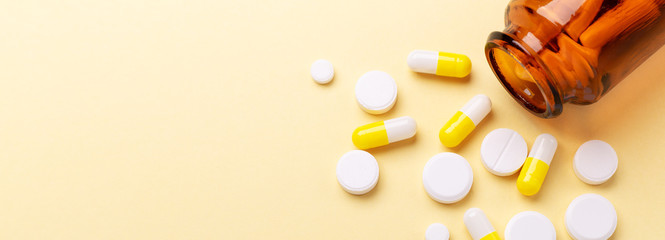 Multicolor tablets and pills capsules from glass bottle on yellow background Heap of assorted...