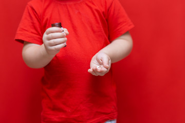 little child boy pours pills from the can into the hand,healthy concept. It is dangerous tablets in babies hands red background