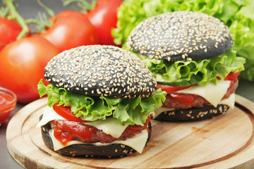 Two black burgers with vegetables and beef meat