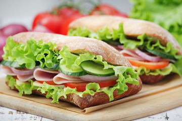 Two sandwiches with fresh vegetables, ham and cheese in ciabatta bread	
